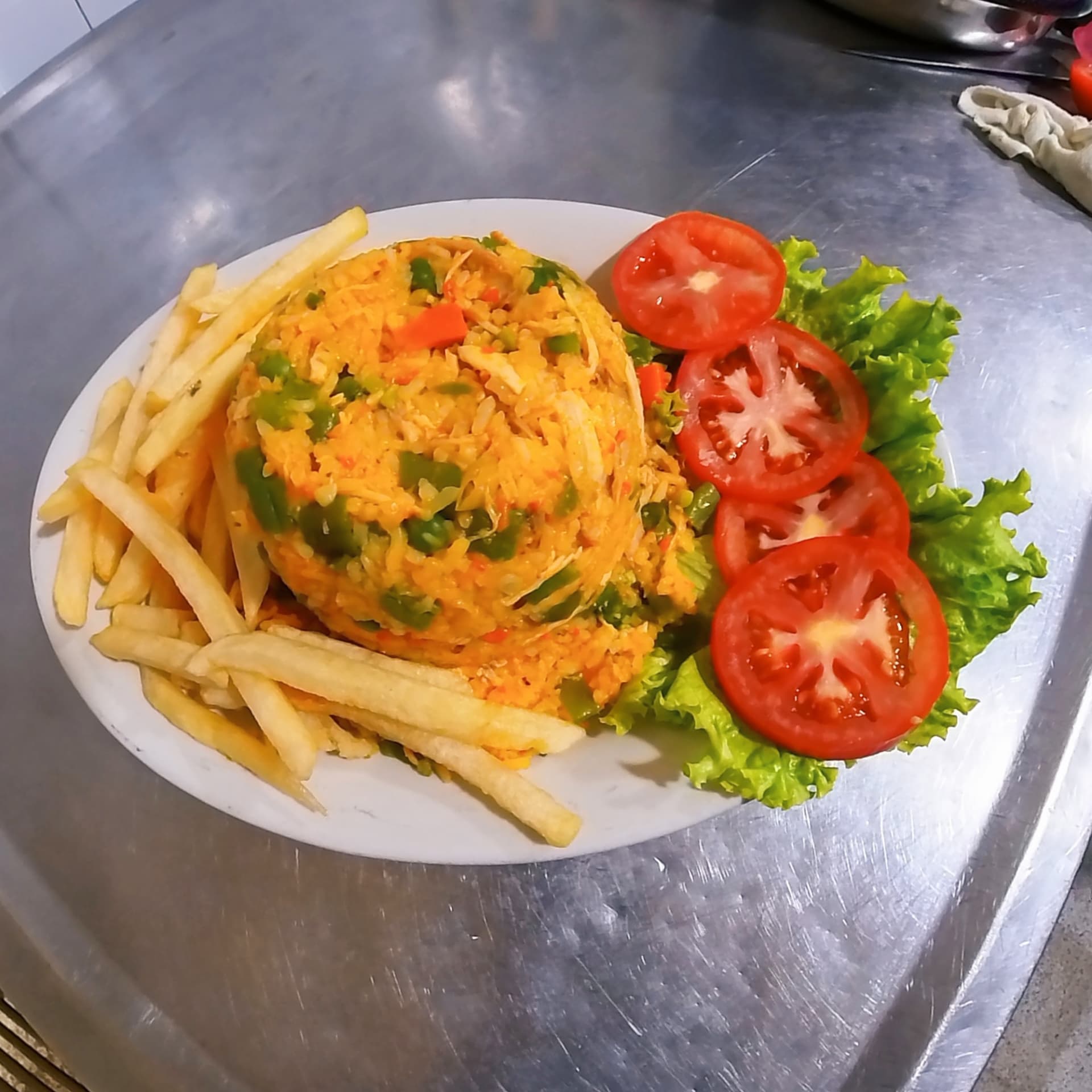 Arroz con pollo servido con papas fritas, tomate y lechuga