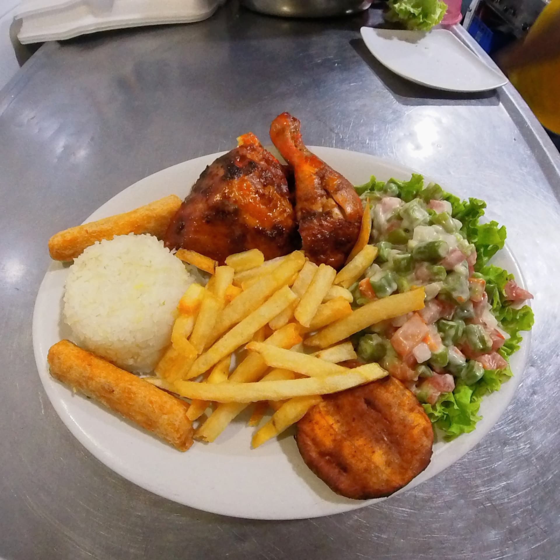 Plato de pollo asado con arroz, papas fritas, yuca y ensalada